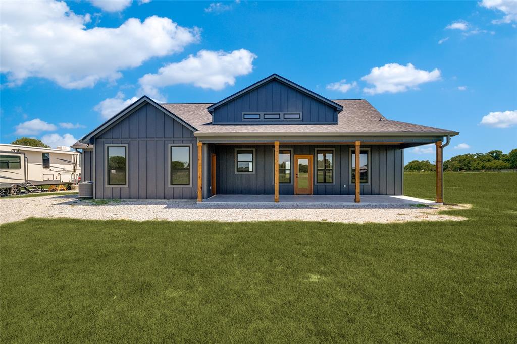 1150 Doss Road Millsap, TX 76066 - Photo 4 of 32 Contemporary farmhouse exterior featuring board and batten siding, an expansive covered patio, a natural wood entry door, and multiple windows with dark trim