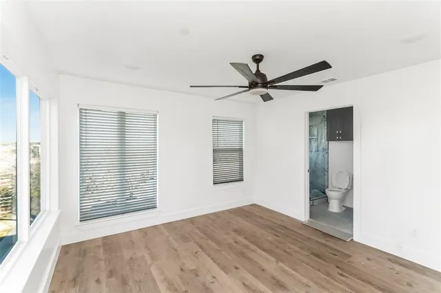 an empty room with wooden floor fan and windows