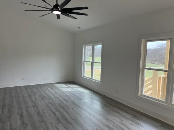 an empty room with wooden floor fan and windows