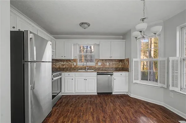 a kitchen with granite countertop a stove a sink and white cabinets with wooden floor