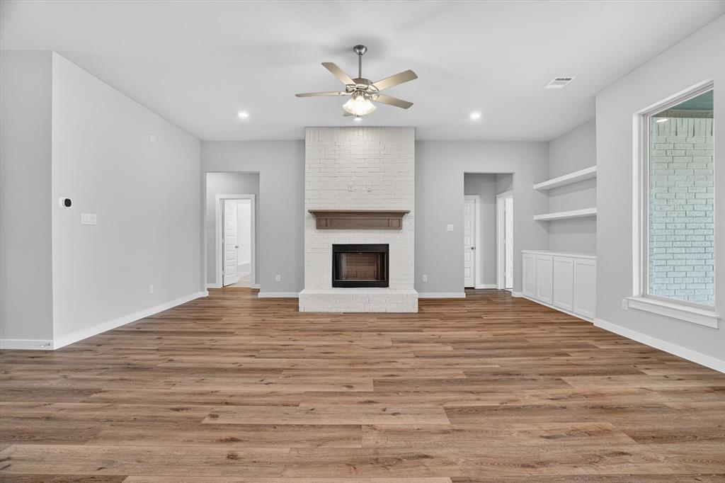 504 Clifton Court Springtown, TX 76082 - Photo 9 of 36 Spacious living area featuring wood-finish flooring, a white brick fireplace with a wood mantle, built-in shelving, white cabinetry, and a ceiling fan