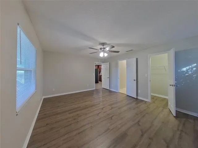 a view of an empty room with wooden floor and a ceiling fan