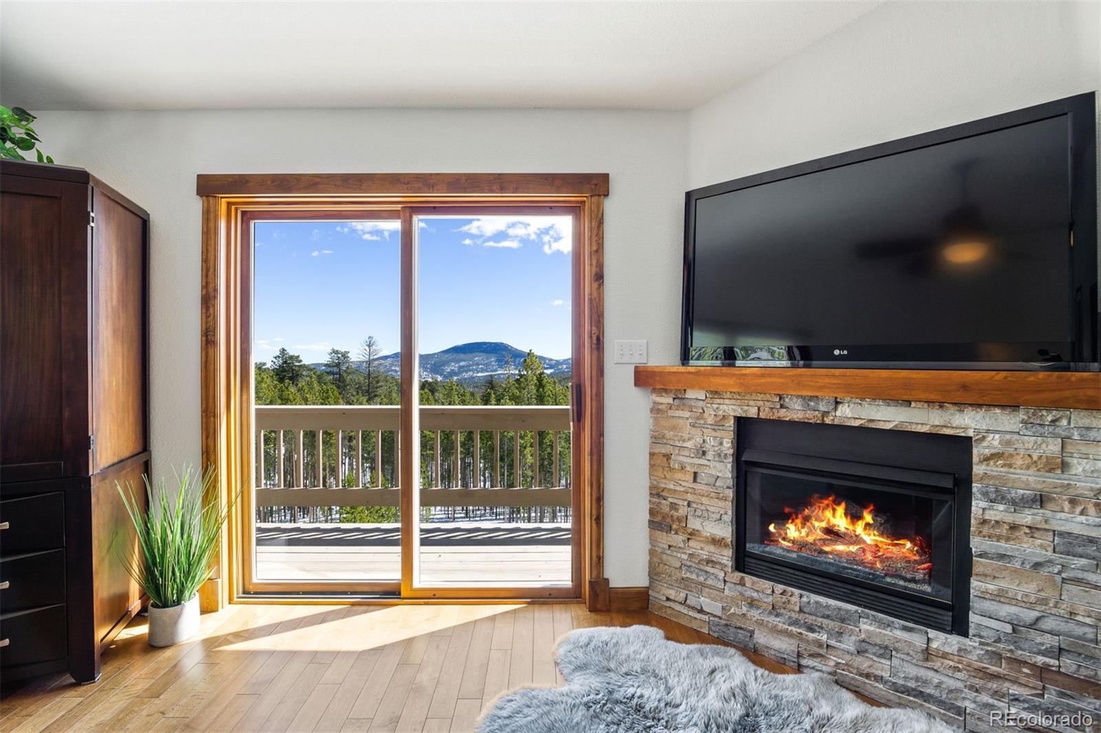 8331 South Warhawk Road Conifer, CO 80433 - Photo 16 of 40 a living room with a fireplace a flat screen tv and a floor to ceiling window