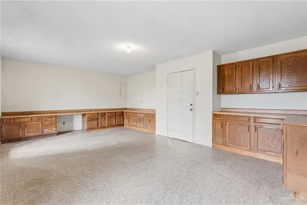 a view of an empty room with kitchen and window