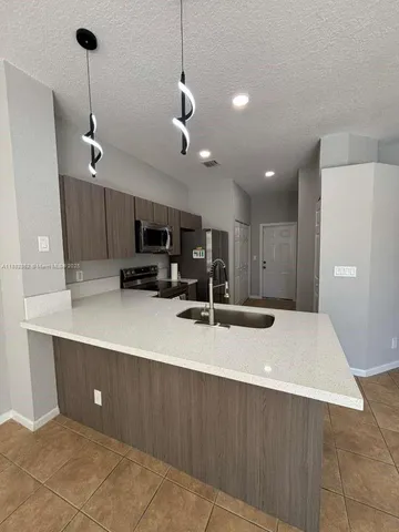 a large kitchen with stainless steel appliances a large counter top a refrigerator and cabinets