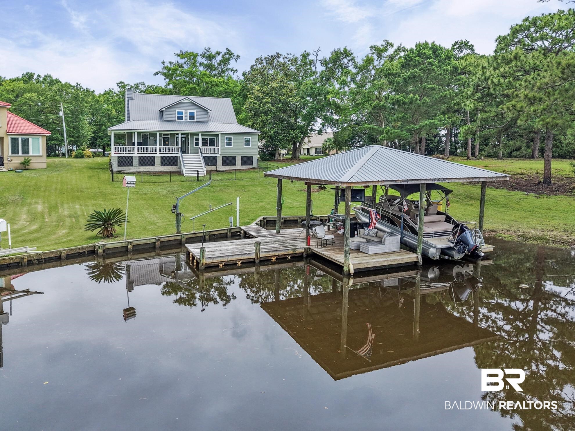12171 Marguerite Drive Coden, AL 36523 - Photo 36 of 44 Waterfront property featuring a covered boat dock with lift, an uncovered pier, and a spacious green lawn