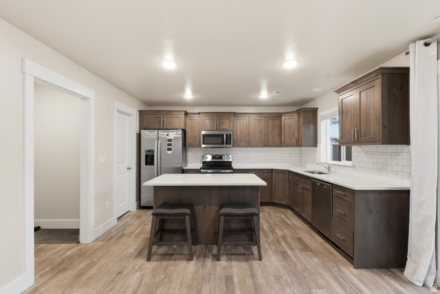 2011 Wren Circle Logan, UT 84339 - Photo 9 of 20 Kitchen featuring light wood-type flooring, appliances with stainless steel finishes, a breakfast bar area, dark brown cabinetry, and a center island