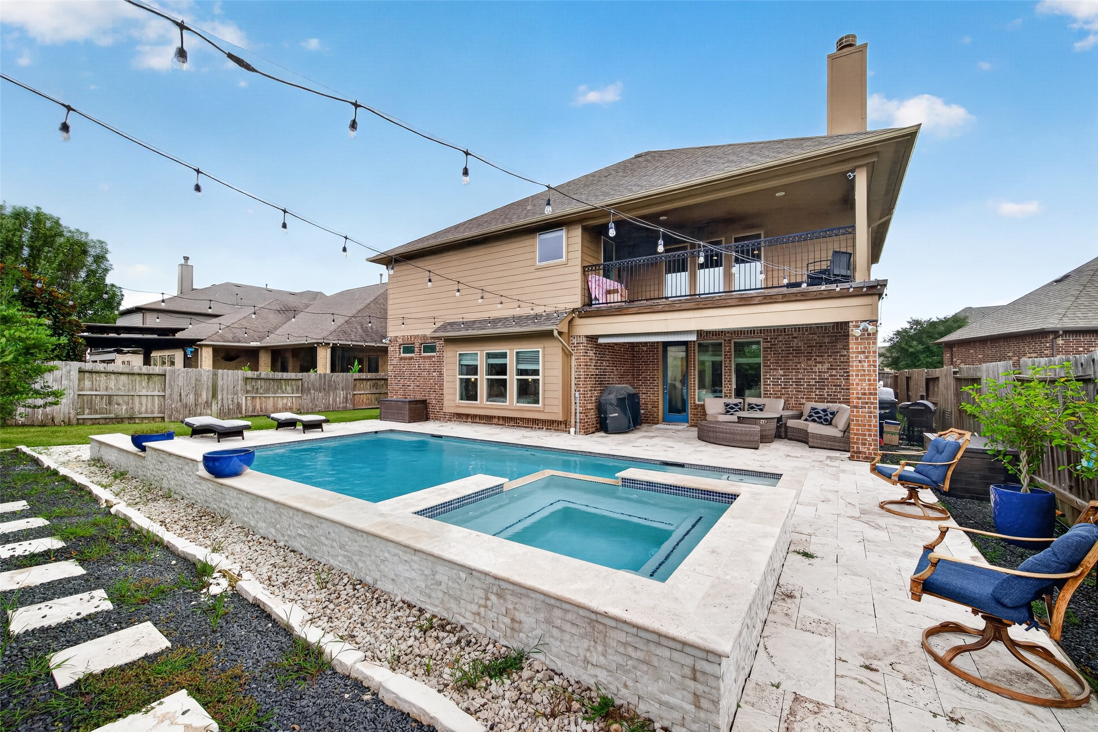 25611 Ellis Ridge Court Katy, TX 77494 - Photo 44 of 49 This photo showcases a spacious backyard featuring a modern swimming pool with an integrated hot tub. The area is ideal for outdoor entertainment, complete with string lights, comfortable seating, and a second-floor balcony. The brick exterior adds a classic touch to this inviting home.