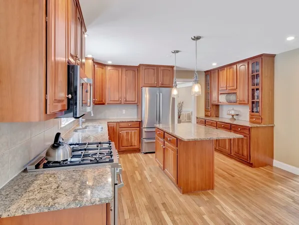 a large kitchen with stainless steel appliances granite countertop a stove a refrigerator a sink dishwasher and wooden cabinets with wooden floor