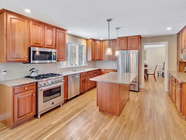 a kitchen with stainless steel appliances a stove top oven a sink dishwasher a refrigerator and a dining table with wooden floor