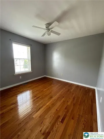 an empty room with wooden floor windows and fan