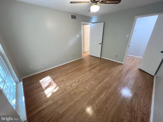 an empty room with wooden floor fan and windows