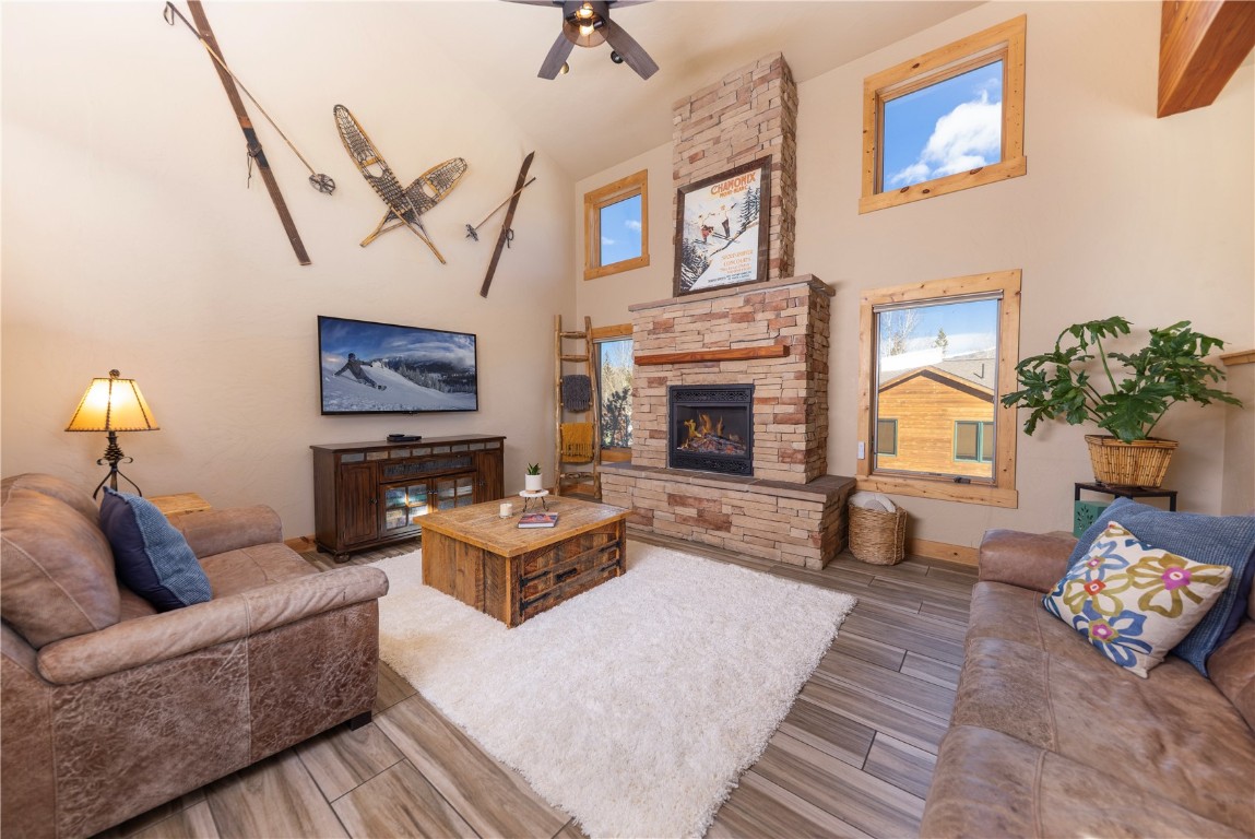 Living area featuring wood finish floors, a high ceiling, a fireplace, and ceiling fan