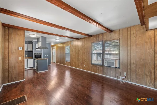 a view of an empty room with wooden floor and a kitchen