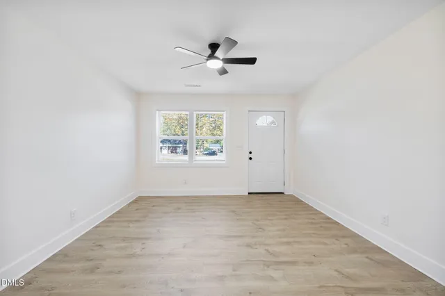an empty room with wooden floor ceiling fan and windows