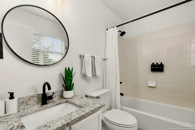 a bathroom with a granite countertop bathtub sink vanity mirror and toilet