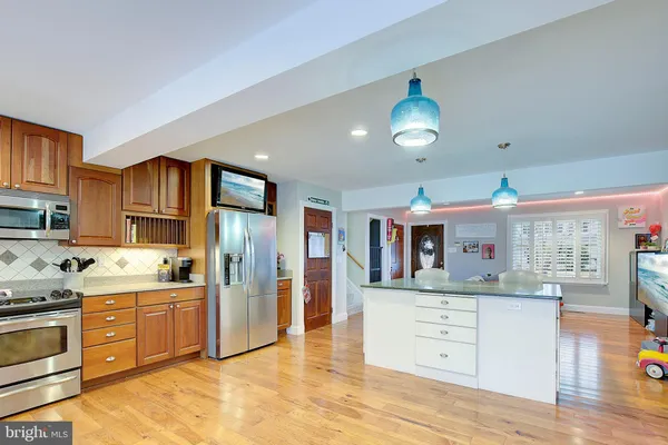 a kitchen with stainless steel appliances kitchen island granite countertop a refrigerator a stove a sink dishwasher and white cabinets with wooden floor