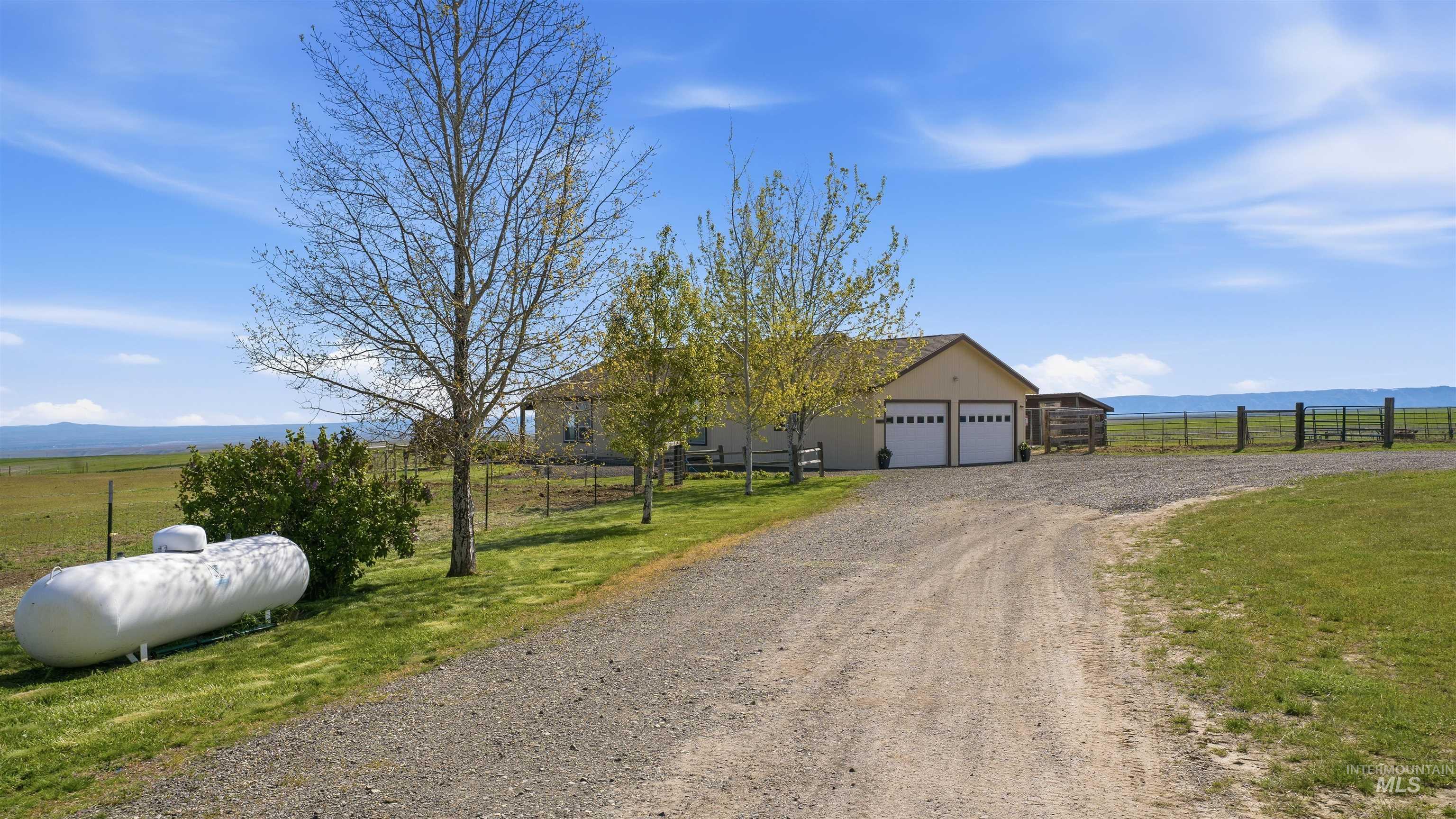 19397 Cloverland Road Asotin, WA 99402 - Photo 28 of 37 Ranch-style residence featuring a two-car garage with white paneled doors, a gravel driveway, and a large propane tank