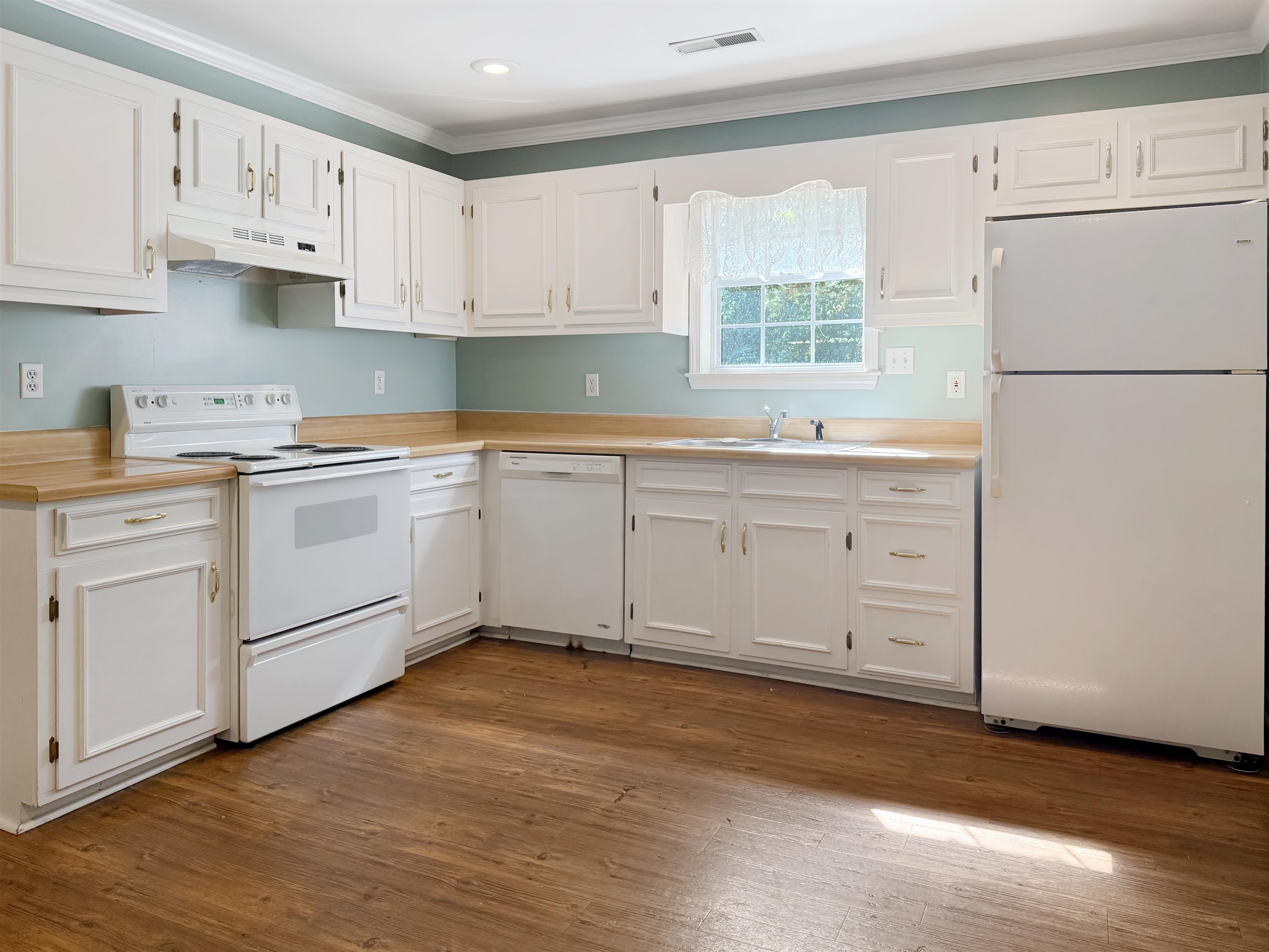 Kitchen featuring white appliances, white cabinets, ornamental molding, light countertops, and under cabinet range hood