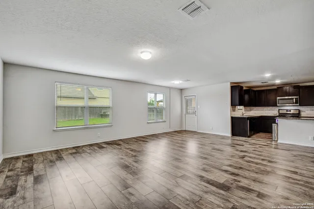 an empty room with kitchen view and wooden floor