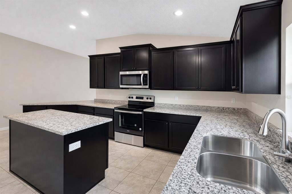7544 Bent Tree Loop St. Cloud, FL 34773 - Photo 5 of 8 a kitchen with kitchen island granite countertop stainless steel appliances a sink stove and refrigerator