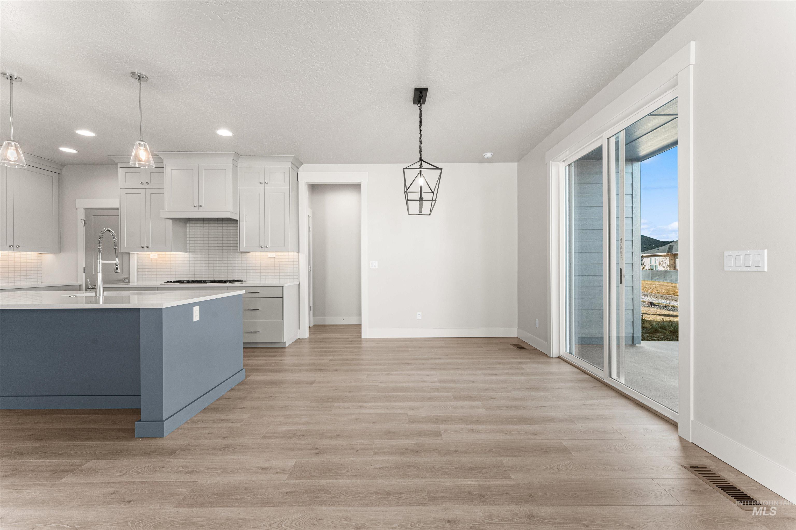 8080 Tandy Cv Street Middleton, ID 83644 - Photo 12 of 35 Kitchen featuring dual tone cabinetry, pendant lighting, light wood finished floors, backsplash, and a breakfast bar