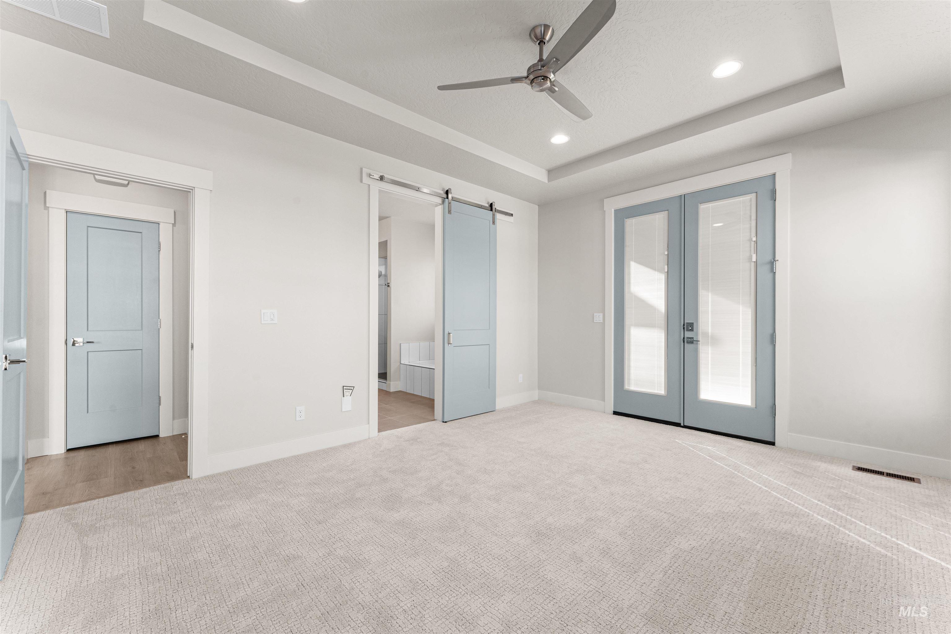 8080 Tandy Cv Street Middleton, ID 83644 - Photo 15 of 35 Unfurnished bedroom with a barn door, a tray ceiling, ensuite bathroom, light carpet, and recessed lighting