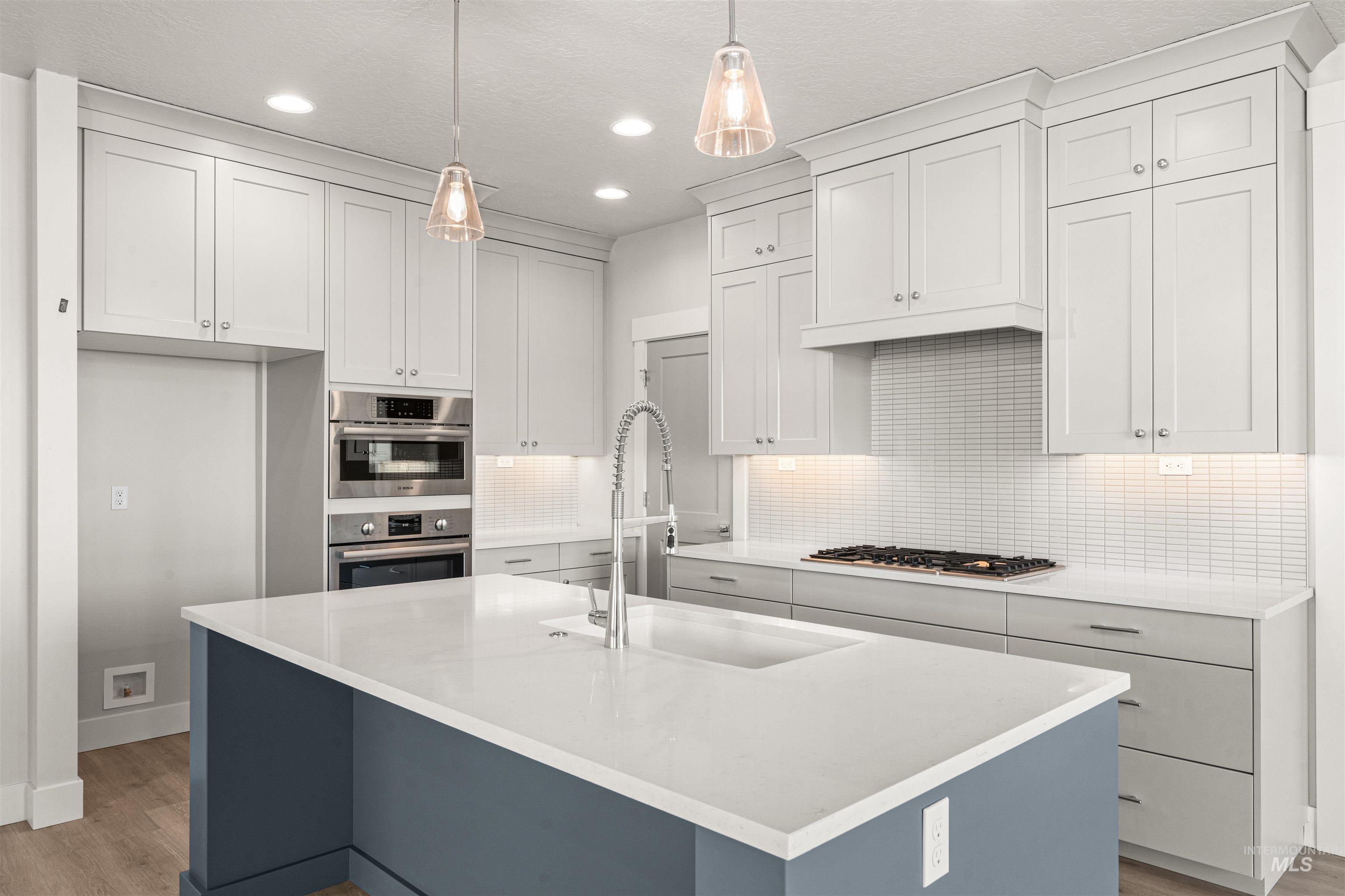 8080 Tandy Cv Street Middleton, ID 83644 - Photo 7 of 35 Kitchen with decorative backsplash, a kitchen island with sink, pendant lighting, light stone countertops, and light wood-style flooring
