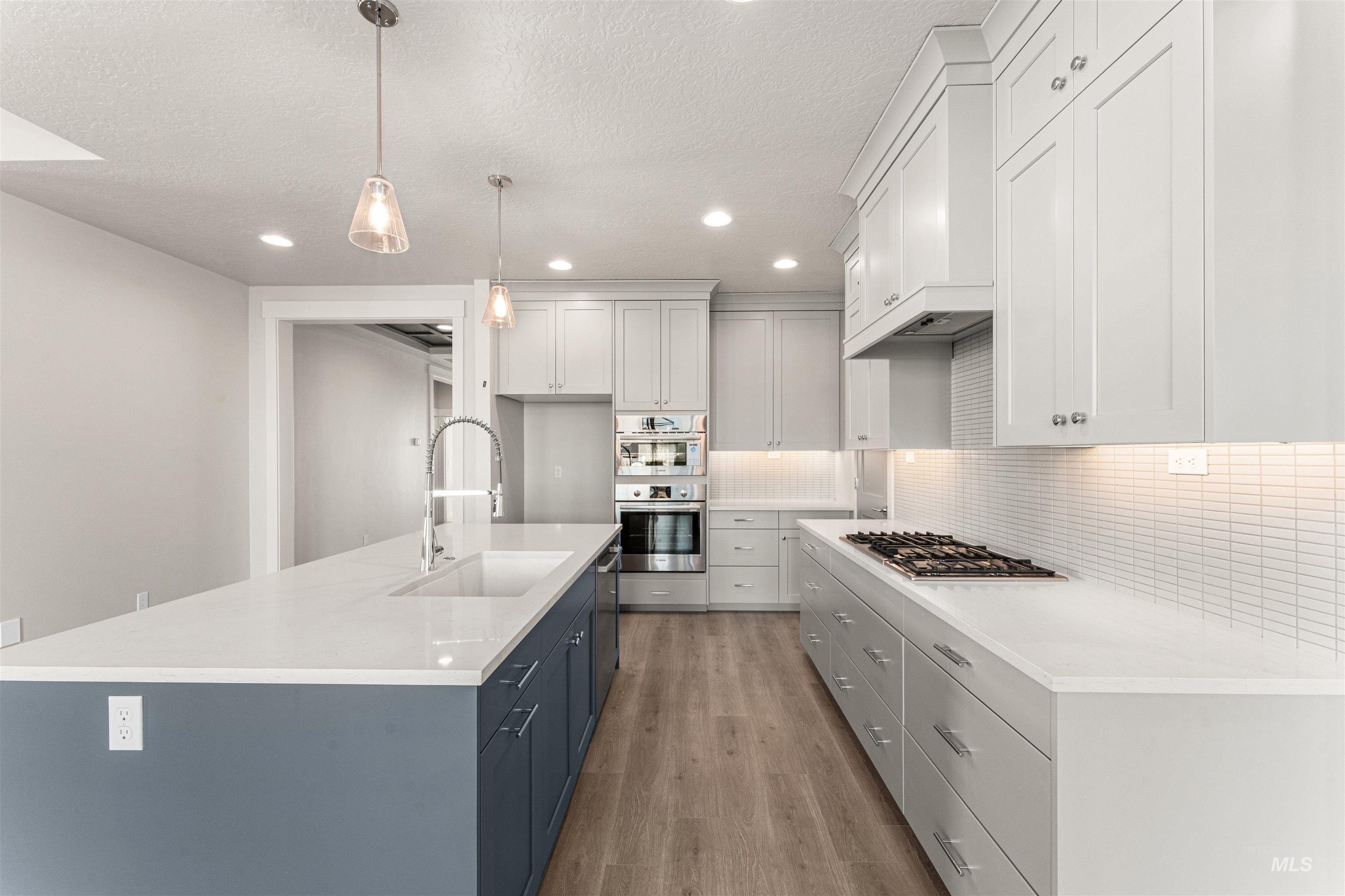8080 Tandy Cv Street Middleton, ID 83644 - Photo 8 of 35 Kitchen featuring two tone cabinets, decorative light fixtures, light wood-type flooring, a center island with sink, and stainless steel appliances