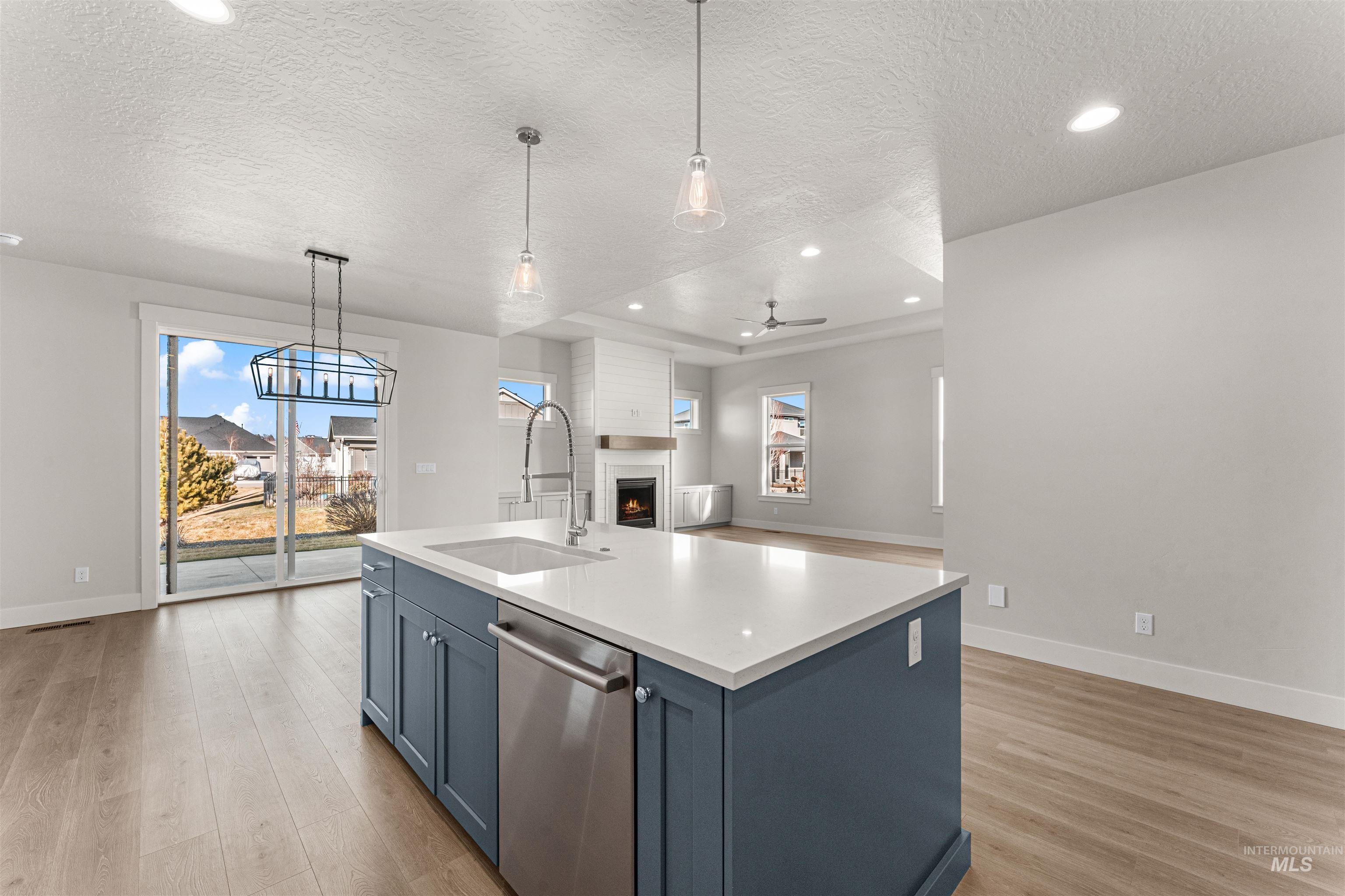 8080 Tandy Cv Street Middleton, ID 83644 - Photo 9 of 35 Kitchen with a lit fireplace, blue cabinets, dishwasher, a textured ceiling, and hanging light fixtures