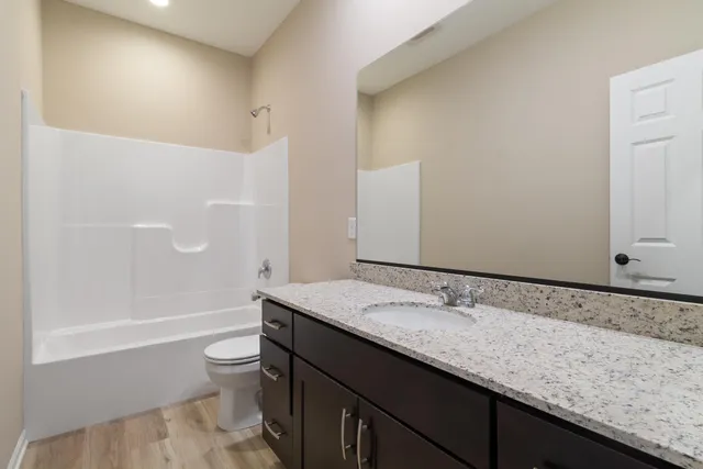 a bathroom with a granite countertop bathtub sink vanity mirror and toilet