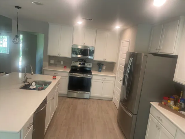 a kitchen with stainless steel appliances a refrigerator a sink a stove and white cabinets