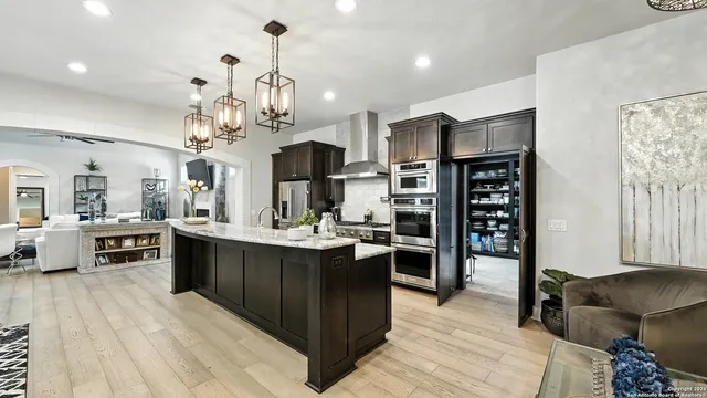 a kitchen with stainless steel appliances kitchen island granite countertop a refrigerator a stove top oven and a dining table with wooden floor