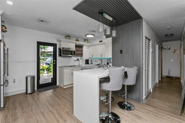 a kitchen with stainless steel appliances granite countertop a refrigerator a sink dishwasher a stove and a dining table with wooden floor