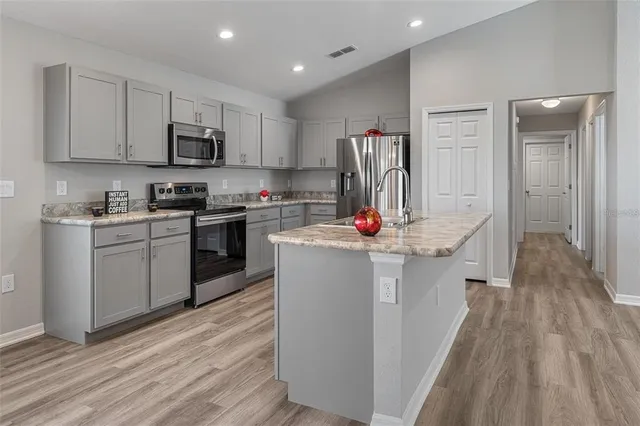 an empty room with wooden floor ceiling fan and kitchen view