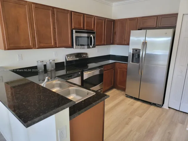 a kitchen with granite countertop a sink a microwave a refrigerator and cabinets