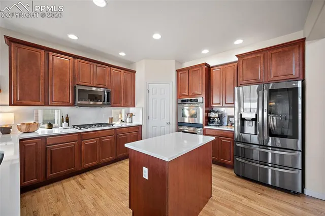a kitchen with stainless steel appliances granite countertop a refrigerator a sink dishwasher a stove top oven a refrigerator with wooden cabinets and wooden floor