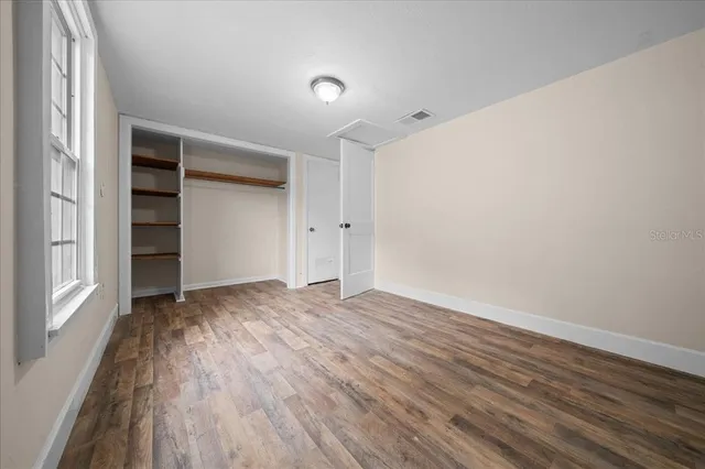 an empty room with wooden floor chandelier fan and windows