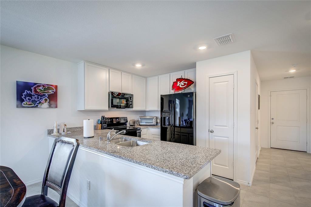 6000 Sumlin Way Princeton, TX 75407 - Photo 11 of 36 Spacious open kitchen with black appliances, a peninsula, light granite countertops, and crisp white cabinetry, enhanced by recessed lighting and abundant prep and storage space.