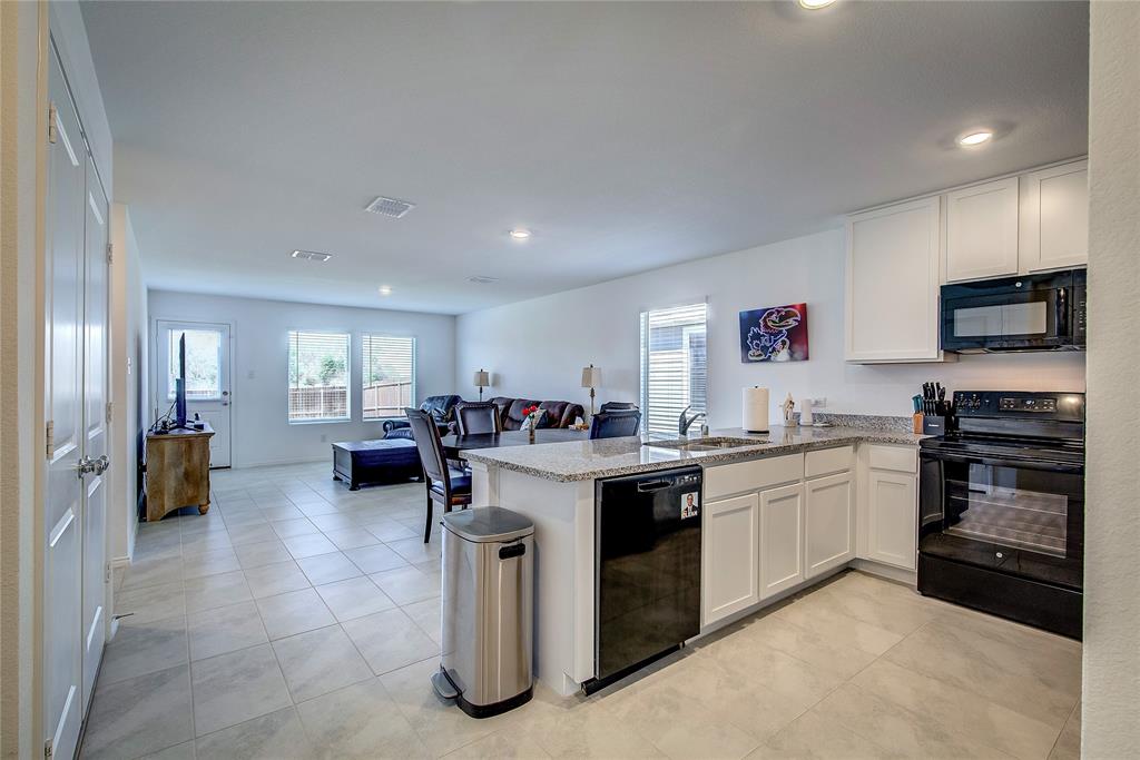 6000 Sumlin Way Princeton, TX 75407 - Photo 9 of 36 Spacious open kitchen with black appliances, a peninsula, light granite countertops, and crisp white cabinetry, enhanced by recessed lighting and abundant prep and storage space.