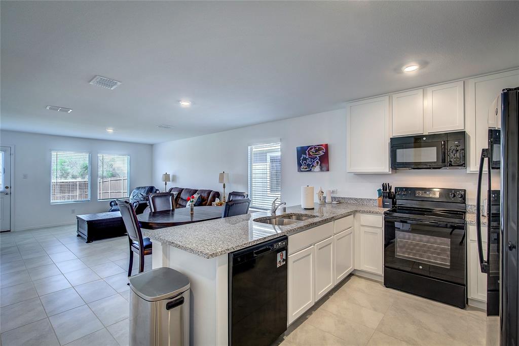 6000 Sumlin Way Princeton, TX 75407 - Photo 10 of 36 Spacious open kitchen with black appliances, a peninsula, light granite countertops, and crisp white cabinetry, enhanced by recessed lighting and abundant prep and storage space.