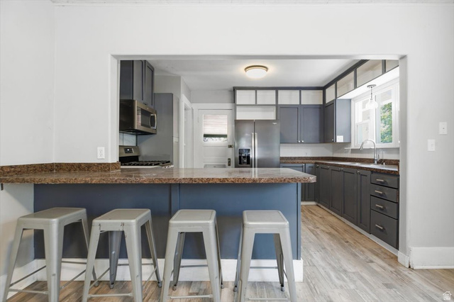 342 North 100 West Logan, UT 84321 - Photo 12 of 23 Kitchen featuring stainless steel appliances, wood-finish flooring, a breakfast bar, gray cabinetry, and a window over the sink