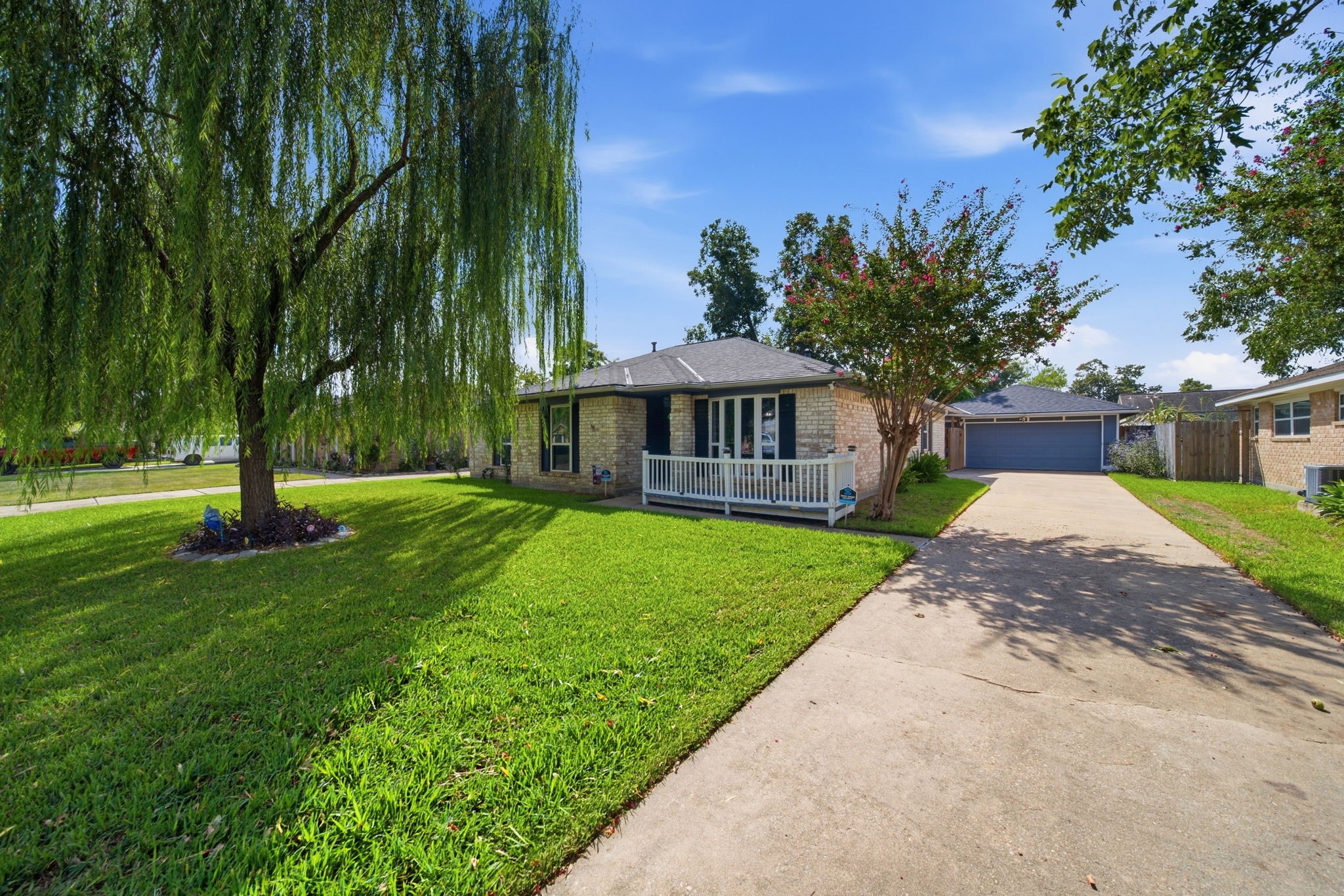 19519 Ricelake Lane Houston, TX 77084 - Photo 3 of 47 Charming brick home with a welcoming front porch, nestled amid lush greenery and mature trees, featuring a long driveway leading to a detached garage.