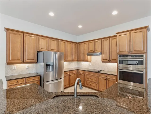 a kitchen with granite countertop a refrigerator stove top oven and sink