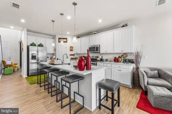 a kitchen with stainless steel appliances kitchen island granite countertop a refrigerator a stove top oven a sink dishwasher and white cabinets with wooden floor