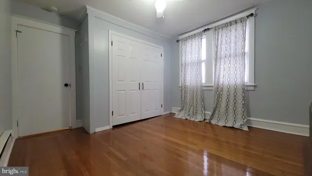 an empty room with wooden floor and windows with curtains