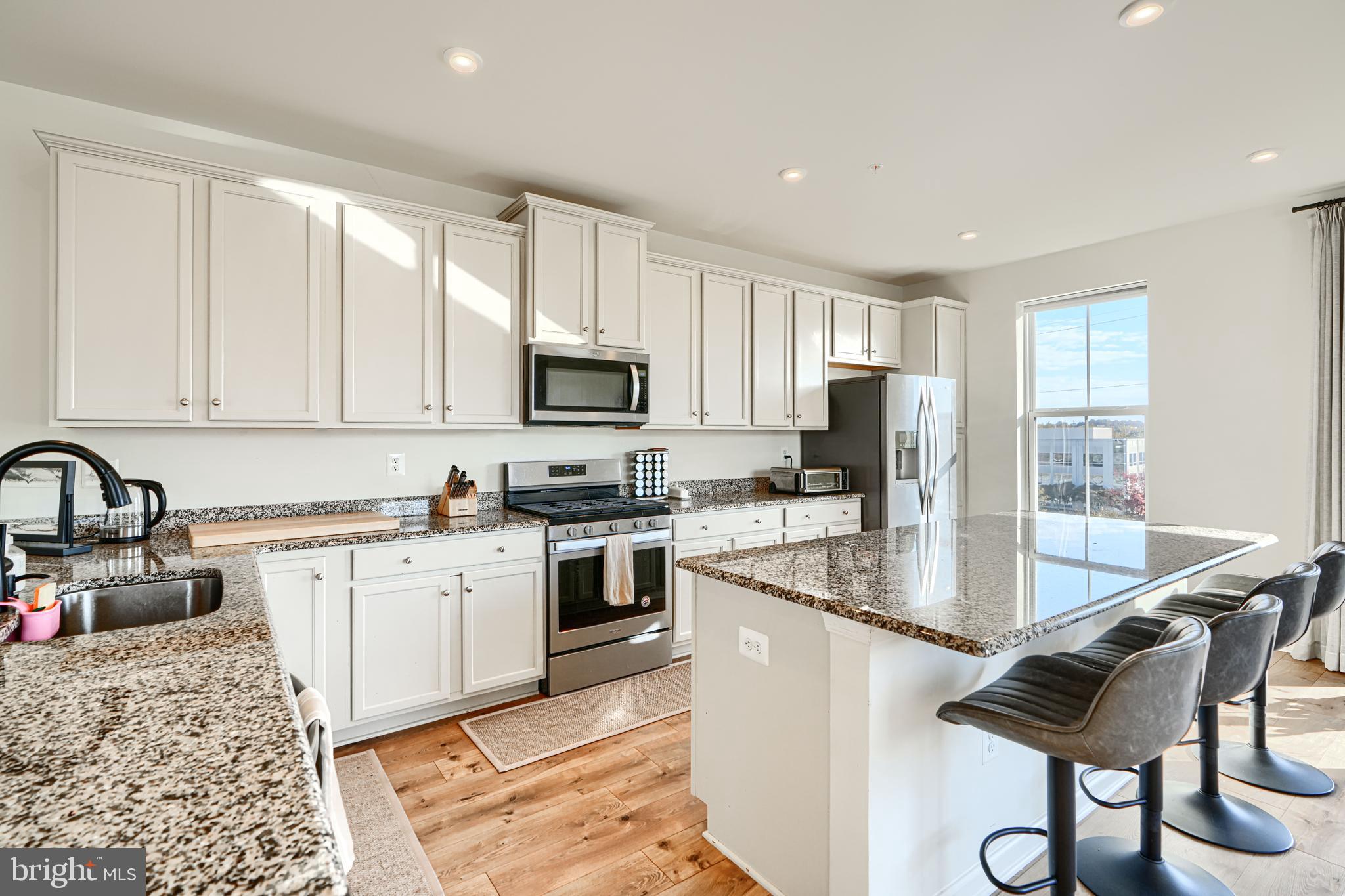 7141 Millstone Road Hanover, MD 21076 - Photo 11 of 32 a kitchen with stainless steel appliances granite countertop a stove top oven a sink dishwasher a dining table and chairs with wooden floor
