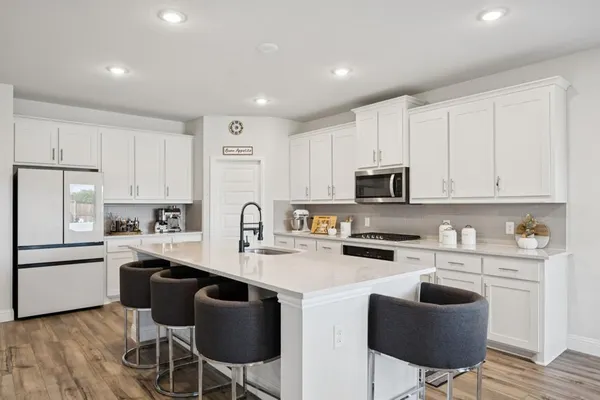 a kitchen with stainless steel appliances granite countertop a stove a sink dishwasher a refrigerator and white cabinets with wooden floor