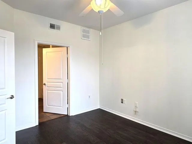 an empty room with a chandelier fan and wooden floor