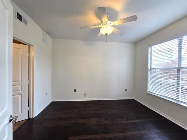 an empty room with wooden floor fan and windows